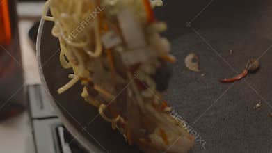 Cooking kitchen throws up a hot frying wok with chicken, vegetables and noodles