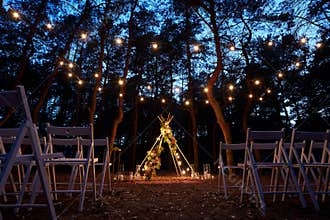 Festive string lights illumination on boho tipi arch decor on outdoor wedding ceremony venue in pine forest at night