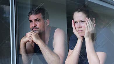 Worried middle aged couple looking through home window