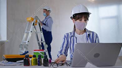 pandemic work, woman designer wearing protective helmet and face mask takes color scheme and looks at camera background