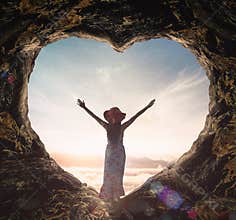 Woman in Floral Dress Celebrating Freedom inside Heart Shaped Cave Viewing Sea of Mist