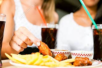 Two women eating chicken wings and drinking soda