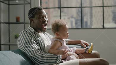 African American father with toddler girl watches TV