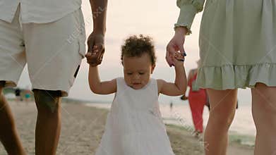 Mixed race toddler girl walks with mom and dad at seaside