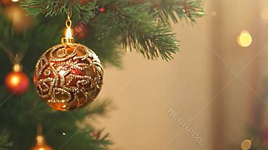 Golden christmas tree ornament hangs from a fir tree branch, shining in the warm light of the holidays. The ornament is
