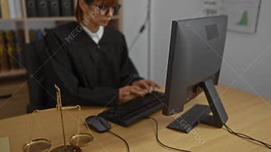 Woman judge working in office on computer with scales of justice on desk, showcasing a professional legal workplace environment