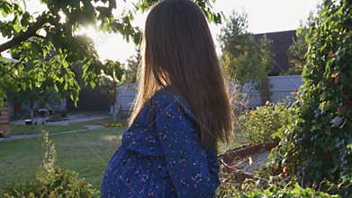 Beautiful pregnant woman enjoying fresh air at sunset rays on the backyard