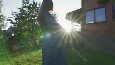 Beautiful pregnant woman enjoying fresh air at sunset rays on the backyard