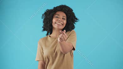 Cute smiling woman with curly hair shows a heart sign with her fingers. A black woman poses against a blue wall and