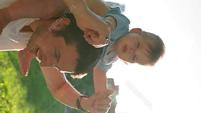 Vertical of Happy father plays with baby holding on shoulders in park