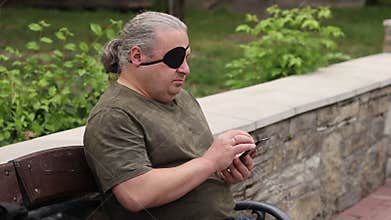 Visually impaired blind man with a black medical patch on his eye looks through the news feed on his phone