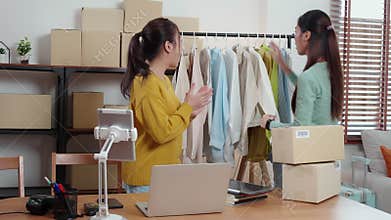 Two young asian woman live online clothing store while showing clothing with tablet on social at home.