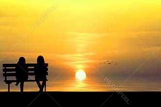 Silhouette of two friends sitting on wood bench near beach