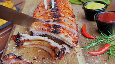 Chef cuts grilled pork ribs with a knife. Cutting board, spices, red yellow sauce, roasted pork ribs.