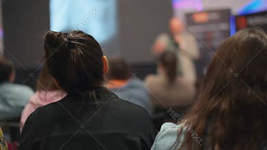 Woman listens attentively to speaker at conference, presenter blurred. Innovative tech presentation captures the