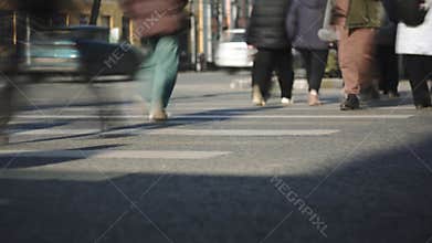 Pedestrians crossing a busy city street at a crosswalk. Low angle shot of feet and legs walking with motion blur. Urban commute