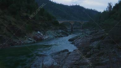 Mountain river with arched bridge among rocks in evening twilight