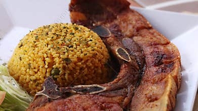 Golden yellow rice served with fried pork chop and fresh lettuce and tomato salad on a white plate