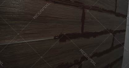 Close-up view of a construction worker's hand carefully applying dark brown grout between wood-effect ceramic tiles on a wall