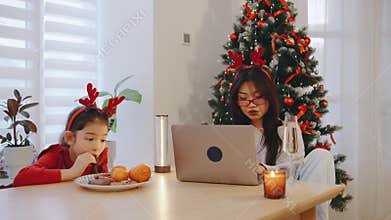 A mother and daughter enjoy Christmas treats at a table by a beautifully decorated tree, creating a warm and festive