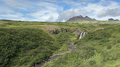 Tiny waterfall in expansive green meadow with distant mountains in Iceland