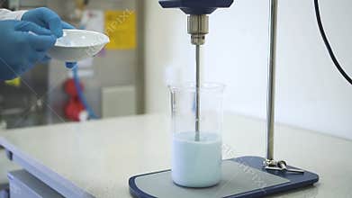 Chemist hand add pour powder to liquid reagent in chemical mixing stirrer in laboratory.