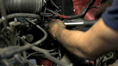 Mechanic with dirty hands tries hard to screw car engine detail with his wrench.