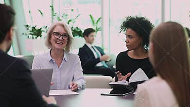 Happy older female leader discussing project details with employees.
