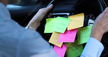 Busy day schedule concept - woman driving car with to do list notes on the wheel