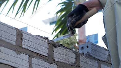 Bricklayer`s hands, male volunteer worker lays brick into wall with cement using trowel, builder man puts the bricks