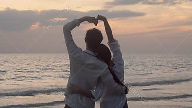 Silhouette of happy asian couple love gesture heart shape symbol of hand on the beach in vacation with romantic together.