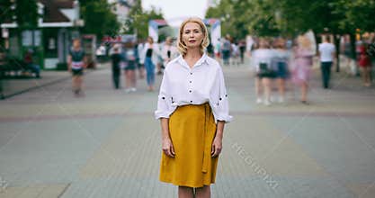 Zoom out time lapse of pretty mature woman looking at camera standing in street