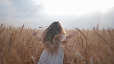 Small female child runs among ripe ears of wheat field against background of blue heaven during harvest season