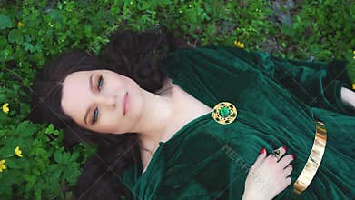 Witch in a emerald raincoat, magician with long curly hairs in spring forest