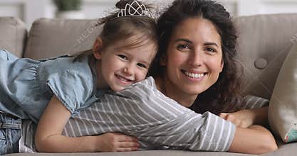 Happy mother and child daughter looking at camera on sofa