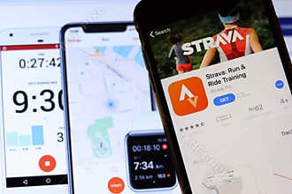 Mobile phone with Strava icon on screen close up with website on laptop. Blurred background with Strava: Run & Ride on itunes