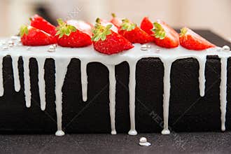Tasty luxury cake for celebration diferrent event. Birthday cake black colored with white glaze and decorated by strawberry