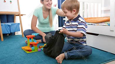 4k video of little smiling boy tidying up his room and putting toys in bag after playing on floor