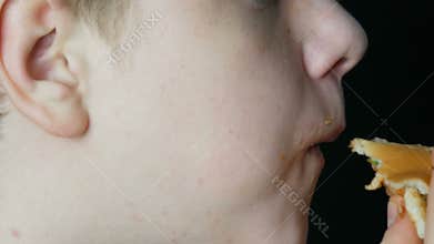The mouth of a teenager boy who eats a juicy burger a cheeseburger or hamburger with cheese, meat cutlet and pickles