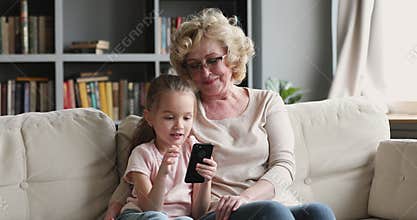 Little granddaughter playing mobile games with granny at home.