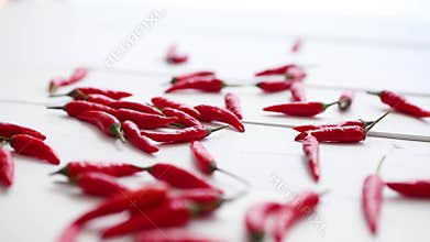 Multiple red chili peppers falling and bouncing at white wooden table in slow motion
