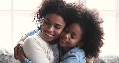 Affectionate young african american mommy cuddling happy biracial teen daughter.