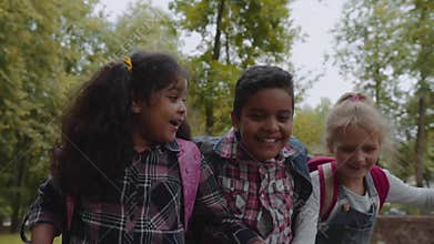 Back to school. Three Friends With Backpacks huging and laughing near school. Mixed Racial Group of School Kids having
