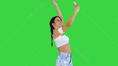 Cute brunette girl takes a selfie and dancing on a green screen, chroma key.