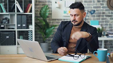 Tired office worker guy is using laptop then taking off glasses touching face