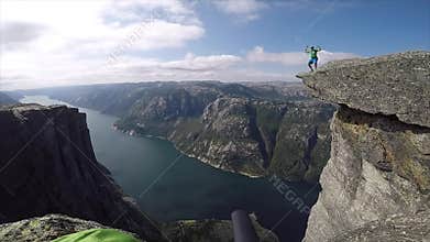Happy man jumping on the edge of high cliff with fjord on background in norway