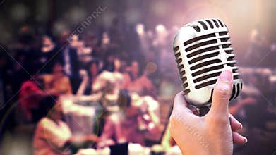 Close up vintage microphone in singer hand singing on stage of wedding event party or business meeting with lighting effect and co