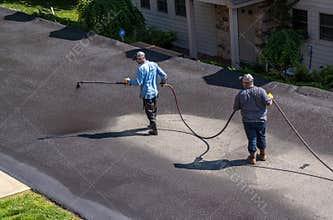 Workers spraying blacktop or asphalt sealer onto roadway