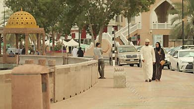 Oriental man and woman in Arabic clothes are walking along city`s promenade.