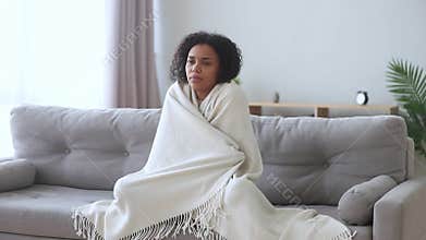 African woman wrapped in plaid shivers with cold at home